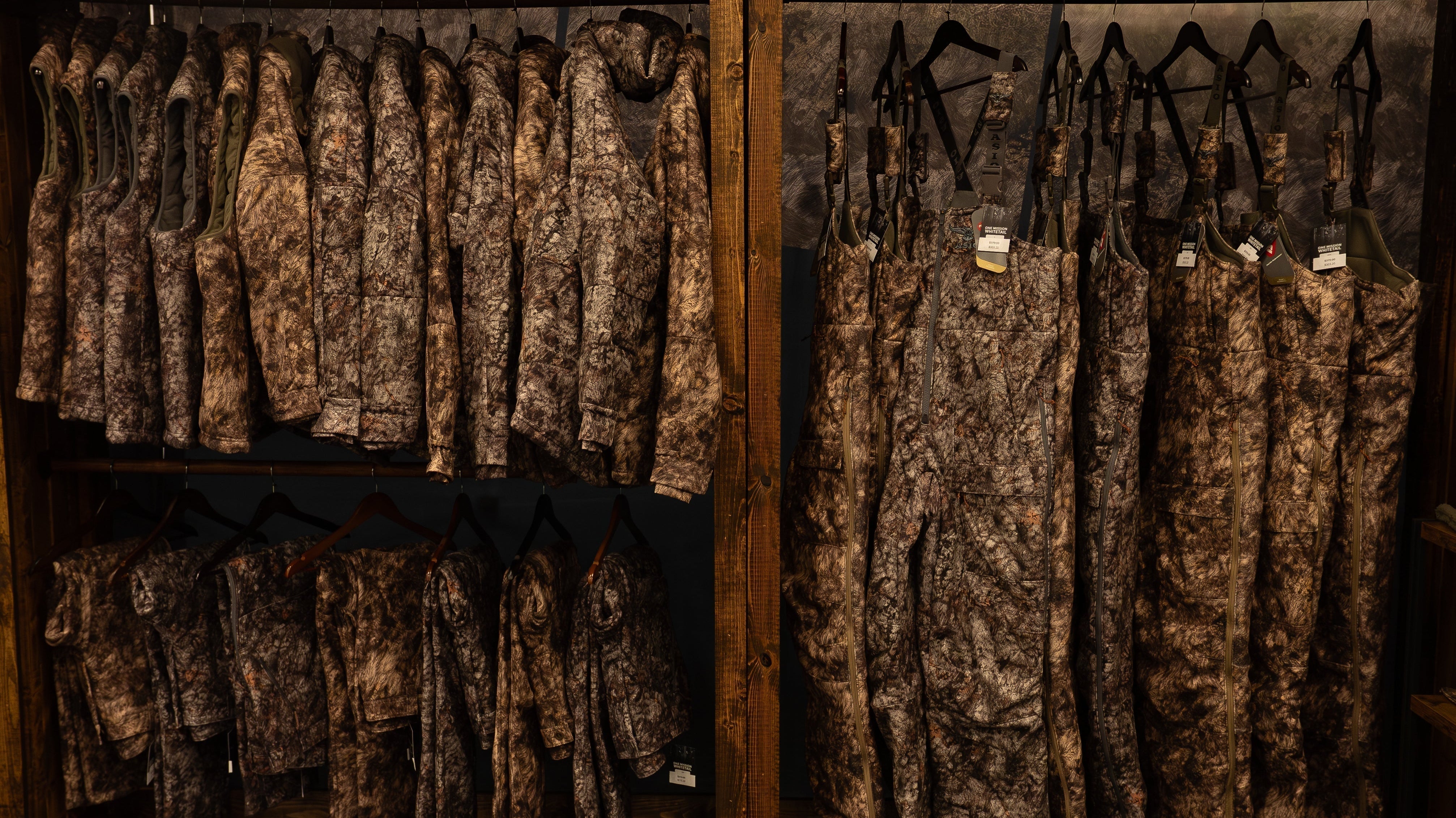 ASIO Gear whitetail bowhunting jackets and bibs displayed at a trade show, showing camo patterns and layering systems up close