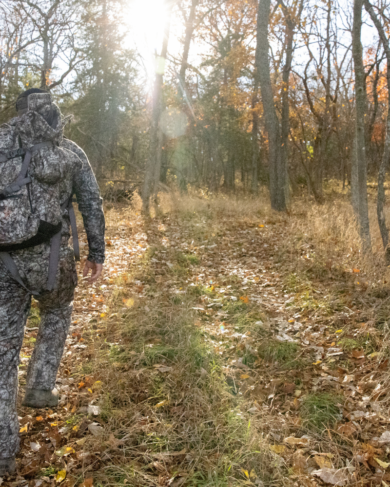 hunter wearing asio gear bowhunting gear walking into woods to hunt during whitetail rut.