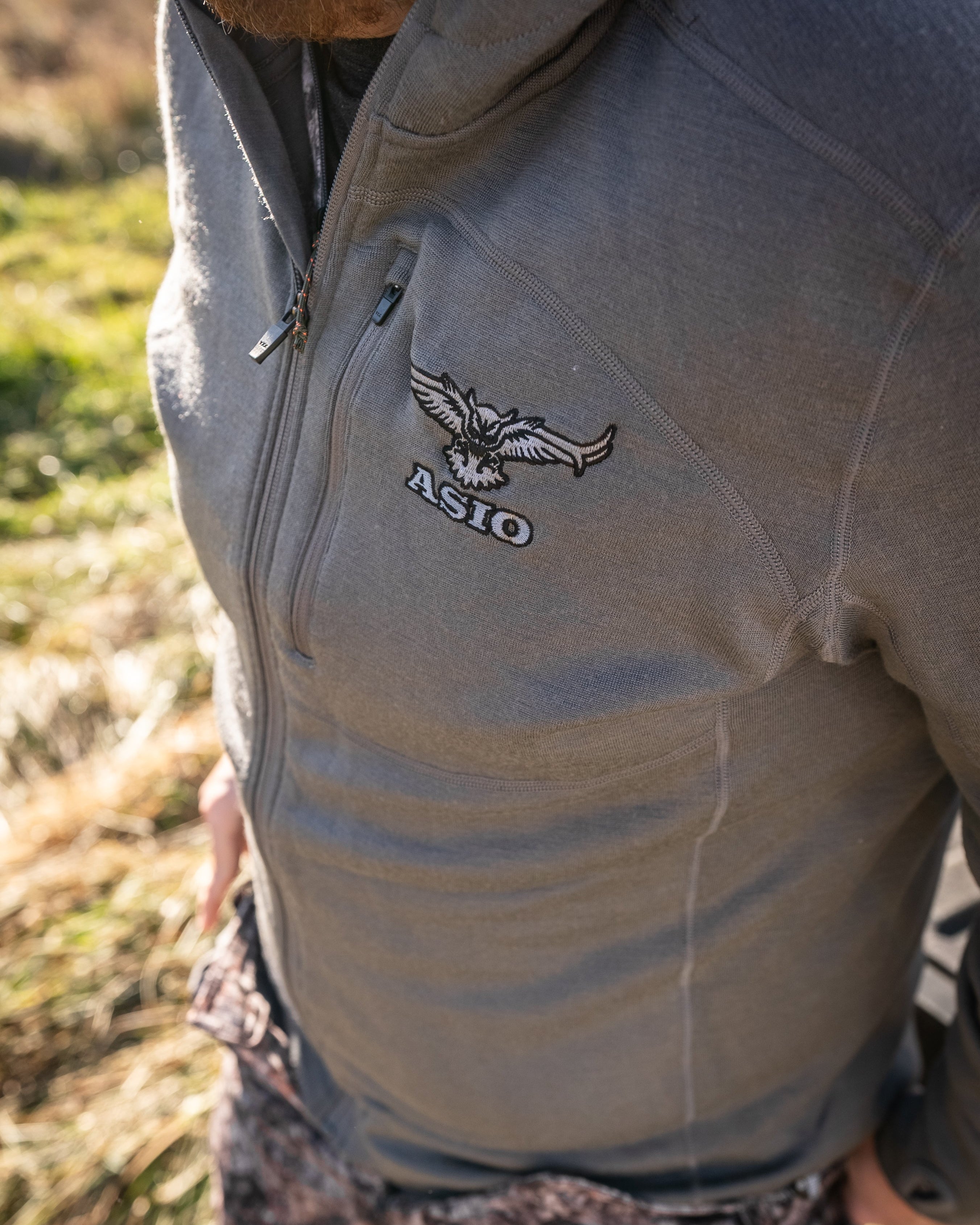 Close-up of a hunter wearing the ASIO Gear Heavyweight Baselayer Top in solid gray, showing the ASIO logo and performance fabric details.