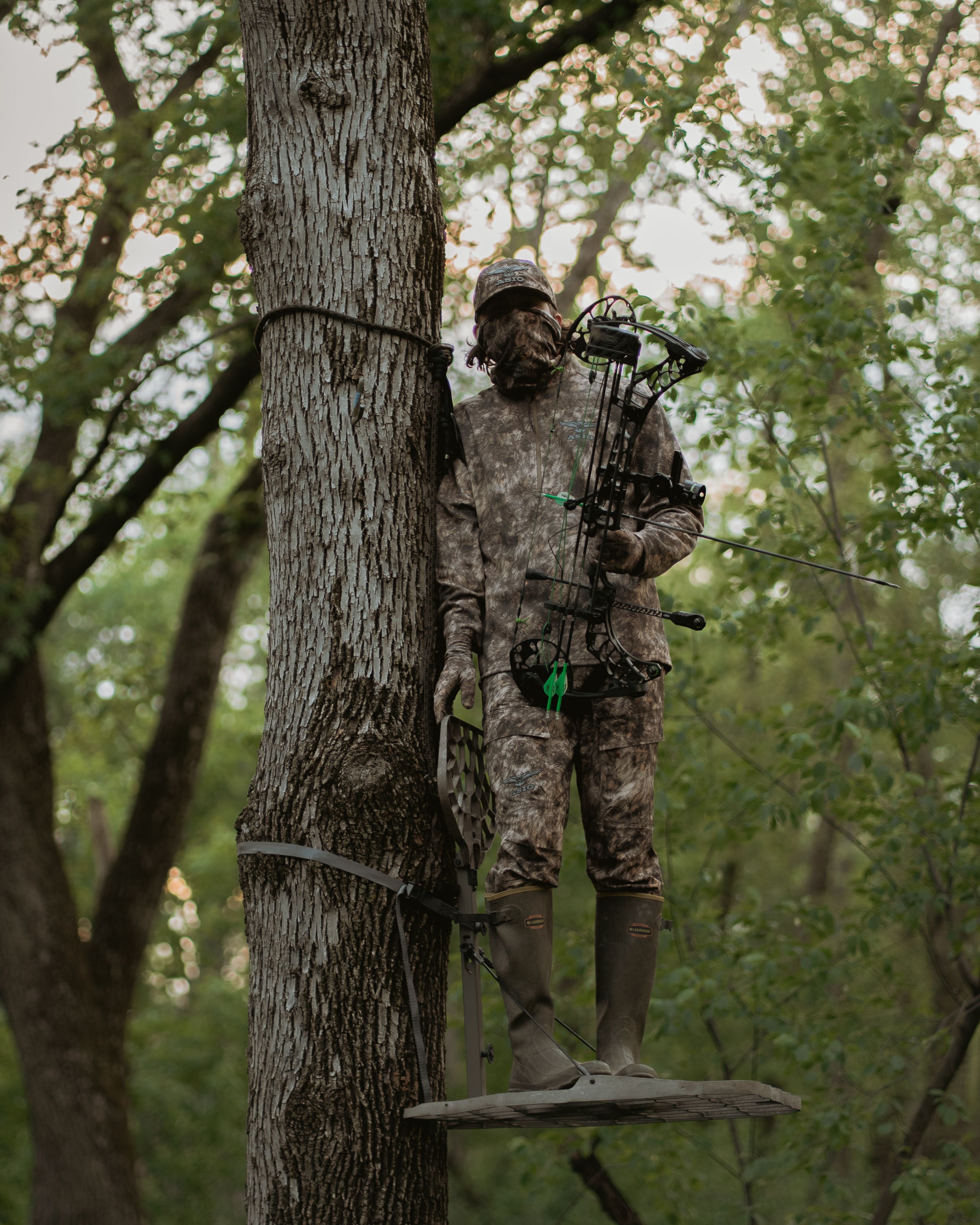 Bowhunter wearing ASIO Gear lightweight pant in RAPX camo standing in a treestand with compound bow at sunrise