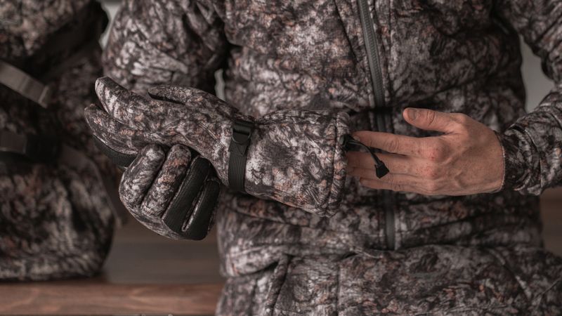 hunter slipping on a heavyweight insulated glove in asio raptor camo.