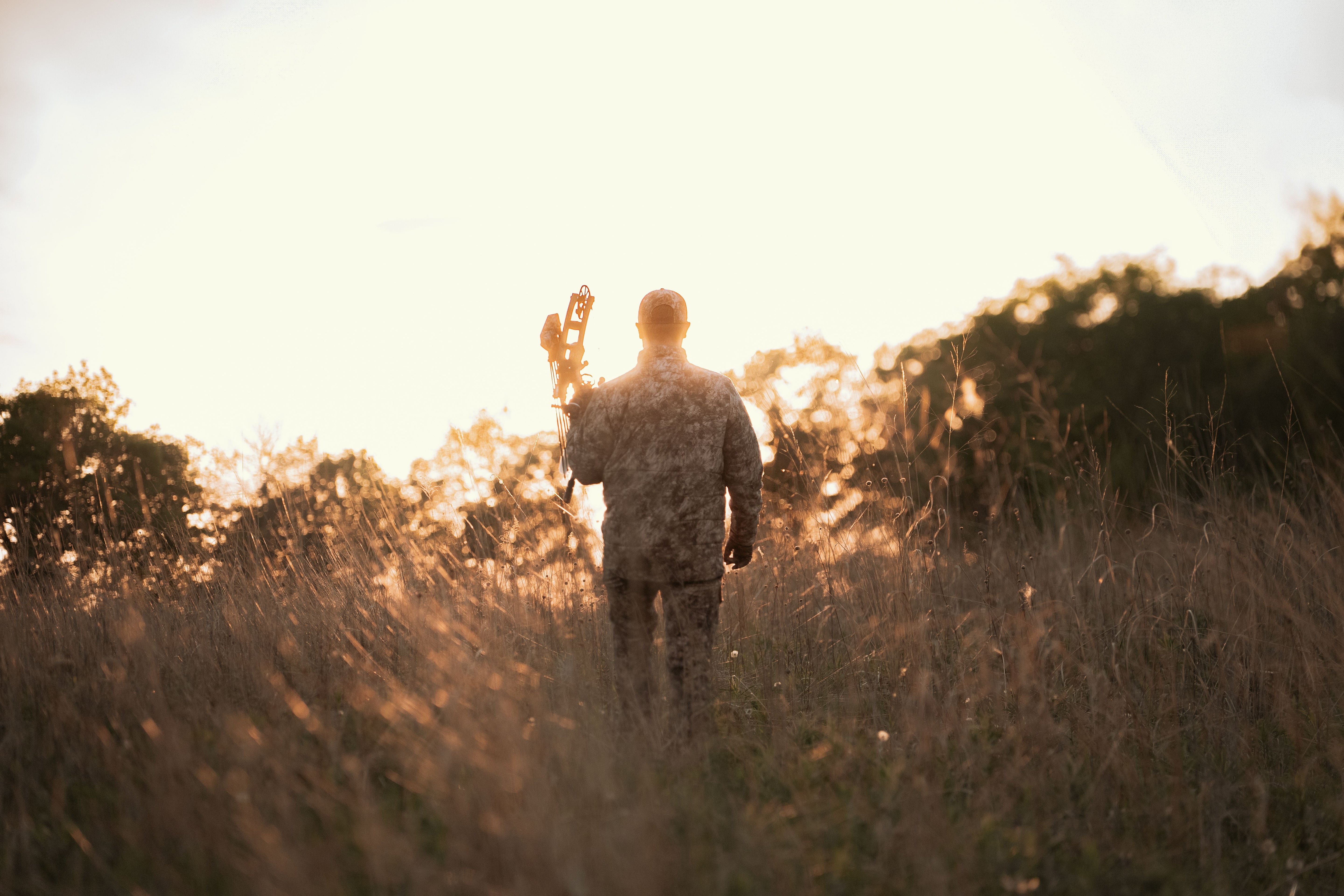 hunter wearing asio gear rapx camo walking into a sunset in a grass field