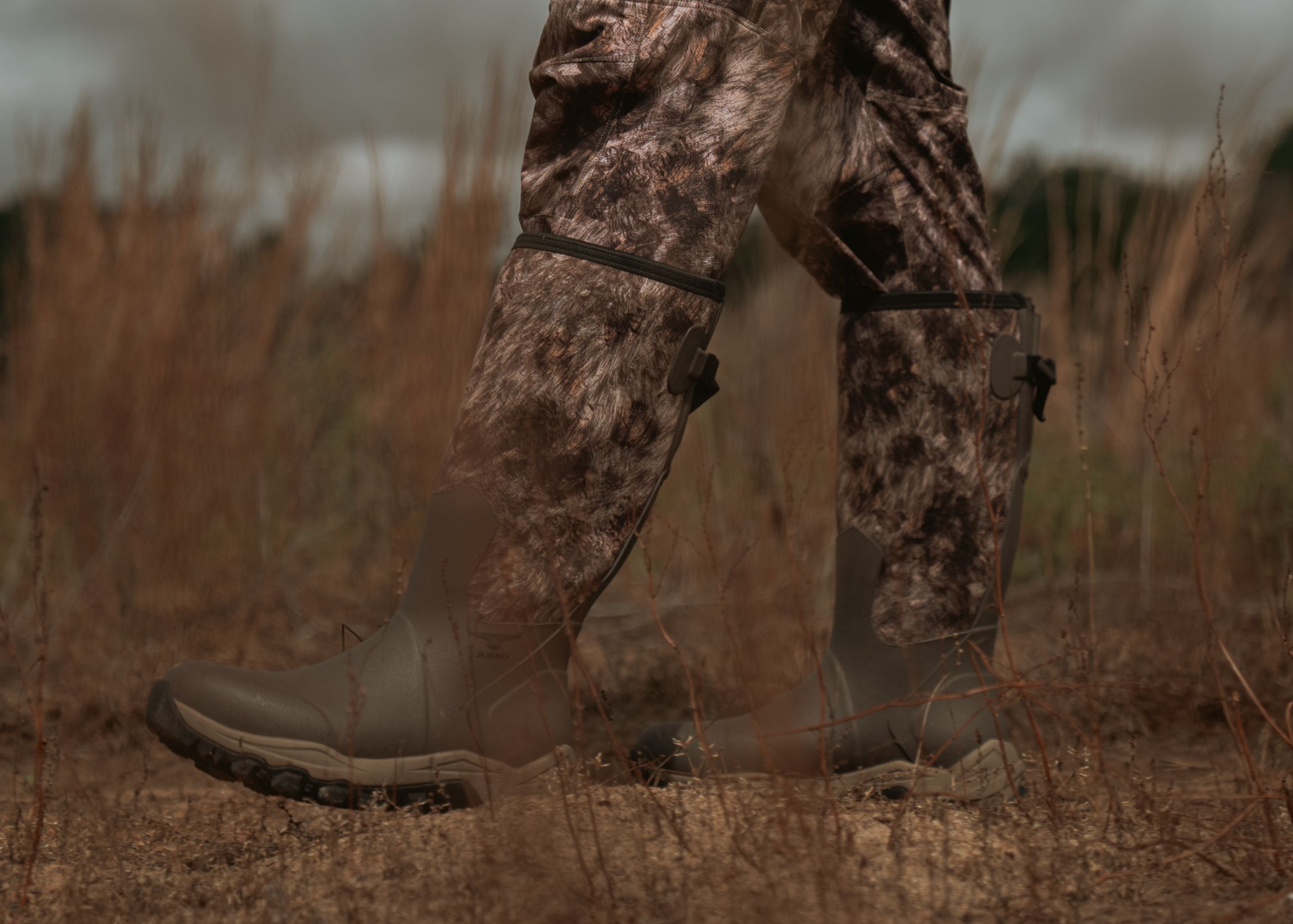 Close-up of ASIO Gear waterproof whitetail pro hunting boots with RAPX camo pants walking through dry field grass, showcasing new 2025 gear release.