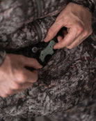 Hunter accessing front zipper pocket of ASIO Gear handmuff in Raptor camo, retrieving a bow release.