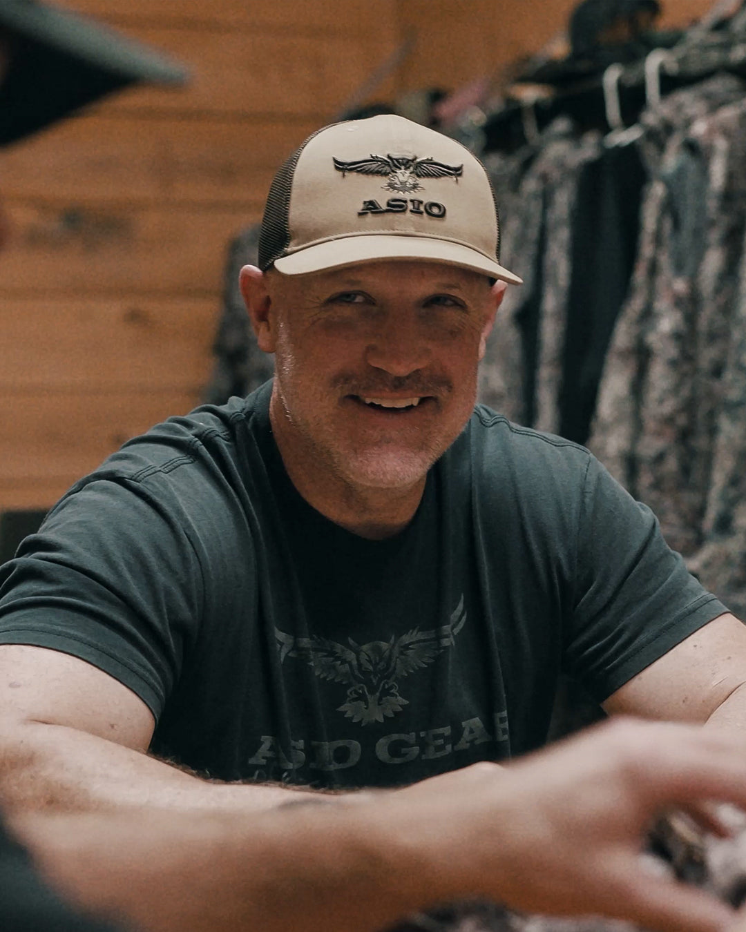 Joe Miles wearing the ASIO Gear brown and khaki trucker hat inside the ASIO showroom.